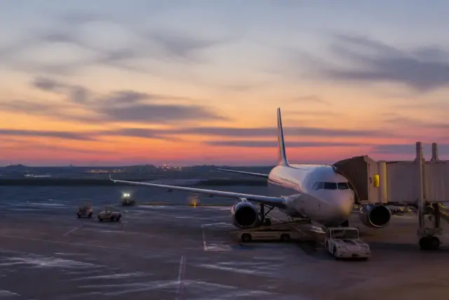 Piste d’aéroport au crépuscule, avion de ligne à l’arrêt près d’une aérogare vitrée, lumières orangées sur le tarmac
