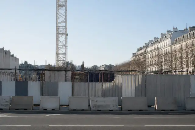 Chantier de gare de métro avec grue et palissades en bord de ville