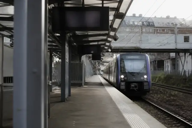 Quai de gare avec un train arrivant et un écran d’affichage des départs