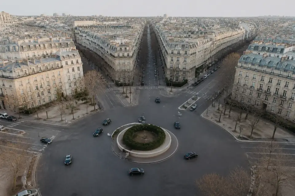 Un grand carrefour giratoire vu de haut, avenues rayonnantes, circulation fluide et ciel clair, sans monument identifiable ni inscription