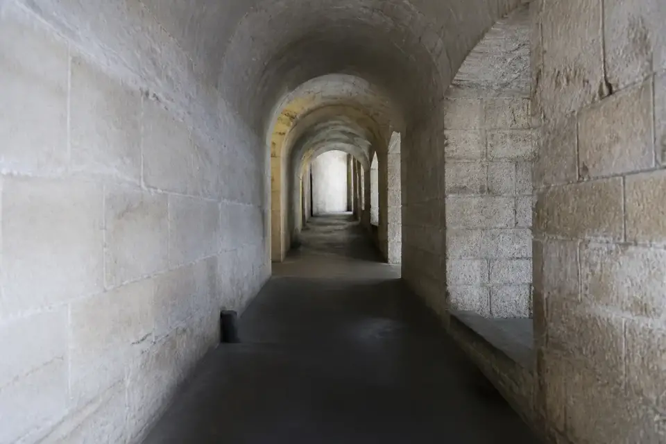 Un étroit couloir de pierre voûté, éclairé par de petites lampes, perspective profonde, sans personne ni inscription
