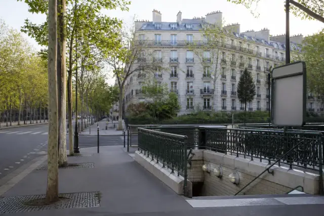 Carrefour parisien avec un boulevard, des arbres et une entrée de métro