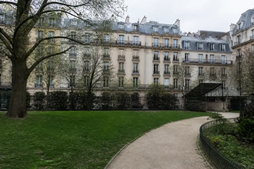 Square paysager avec pelouse, allée et immeubles de pierre en arrière-plan